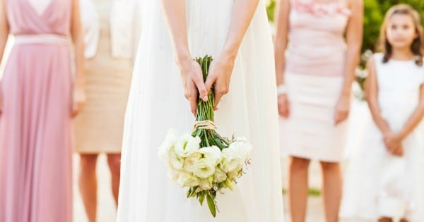 Midsection of bride holding flower bouquet with bridesmaid and flower girl standing in background. Horizontal shot.