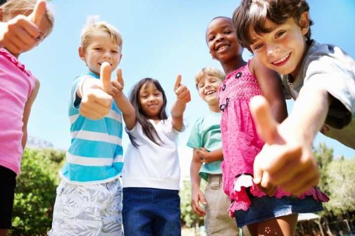 Low angle view of cute kids standing outdoors and giving thumbs up