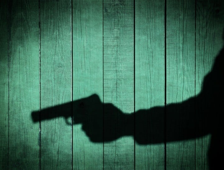 Man in the Shadows with handgun, on natural wooden background, with space for text or image.