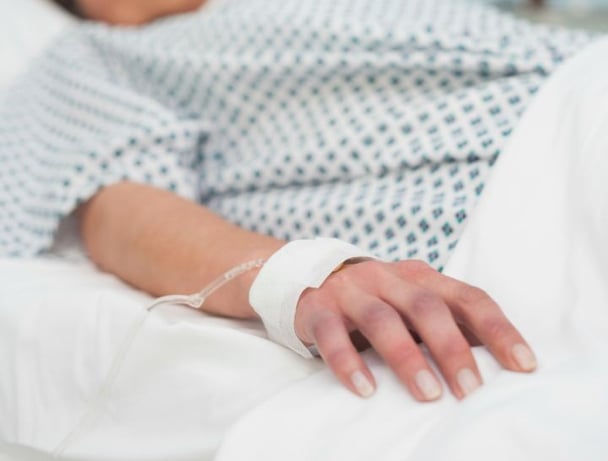 Focus on the hand of a patient lying on a medical bed in hospital ward