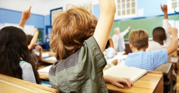 Rear view of a redhead school boy raising his hand in the classroom