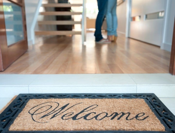 Happy young couple standing inside their new house with a welcome mat at the front door