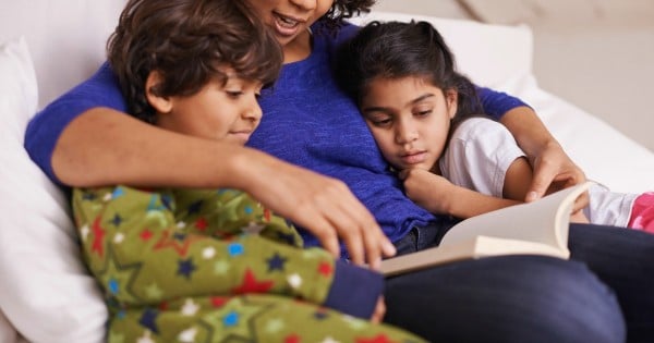 A young mother reading to her children while relaxing at home