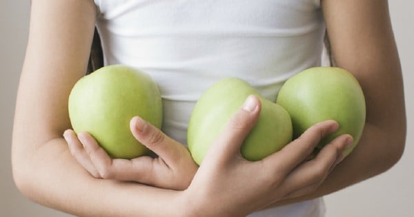 Girl in shirt holding three green apples