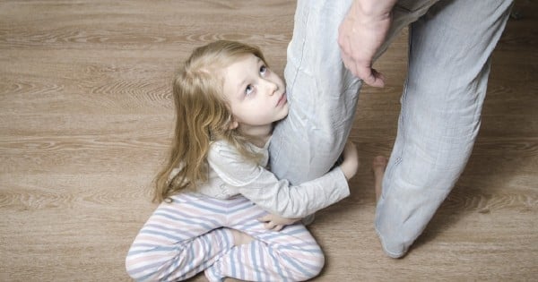 Sad little girl sitting on the floor and hugging her father's leg, top view