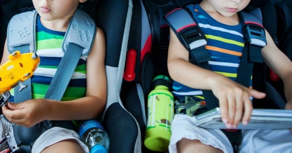 Two boy in children car seats, traveling by car and playing with toys and tablet, summertime