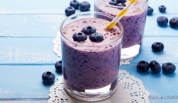 Two glasses of blueberry smoothie on blue colored wooden table