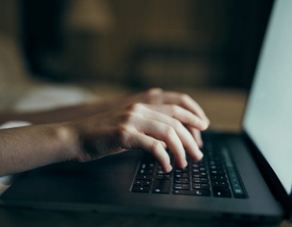 Hands of Caucasian woman typing on laptop in bed