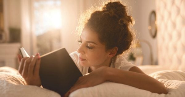 Young woman lying in bed and reading a book.