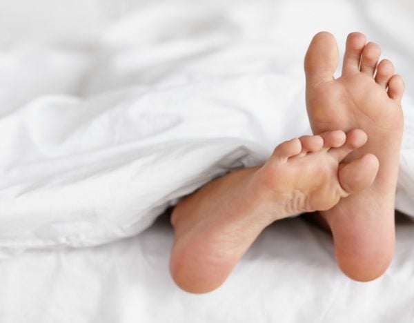 Shot of a pair of woman's feet poking out from under the sheets of a bed.